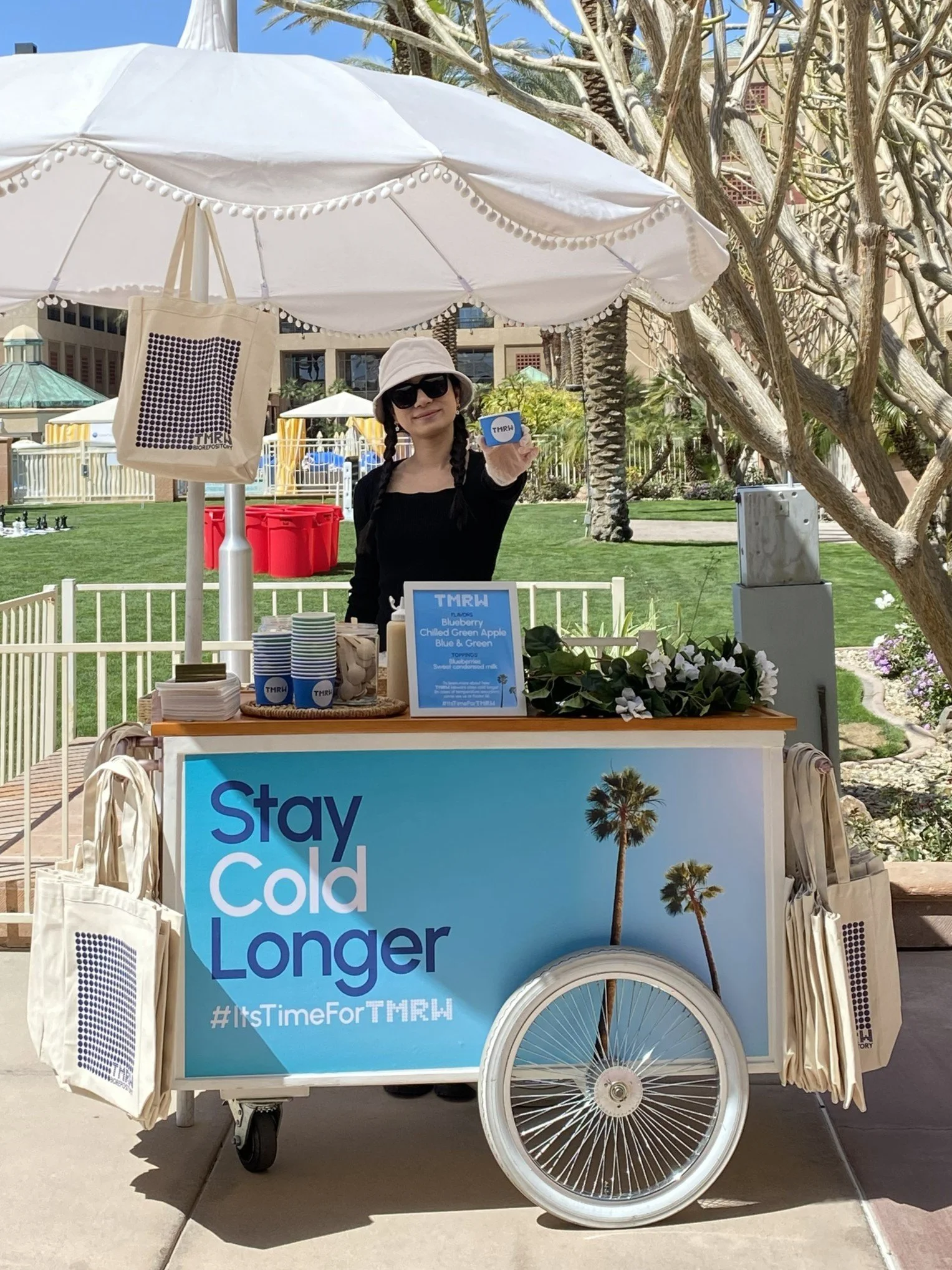 A girl with a bucket hat serving behind a shaved ice cart