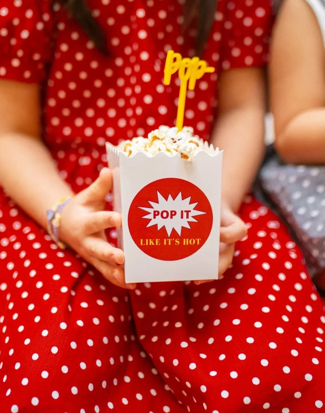 Two small hands holding up one popcorn box with a round label on it