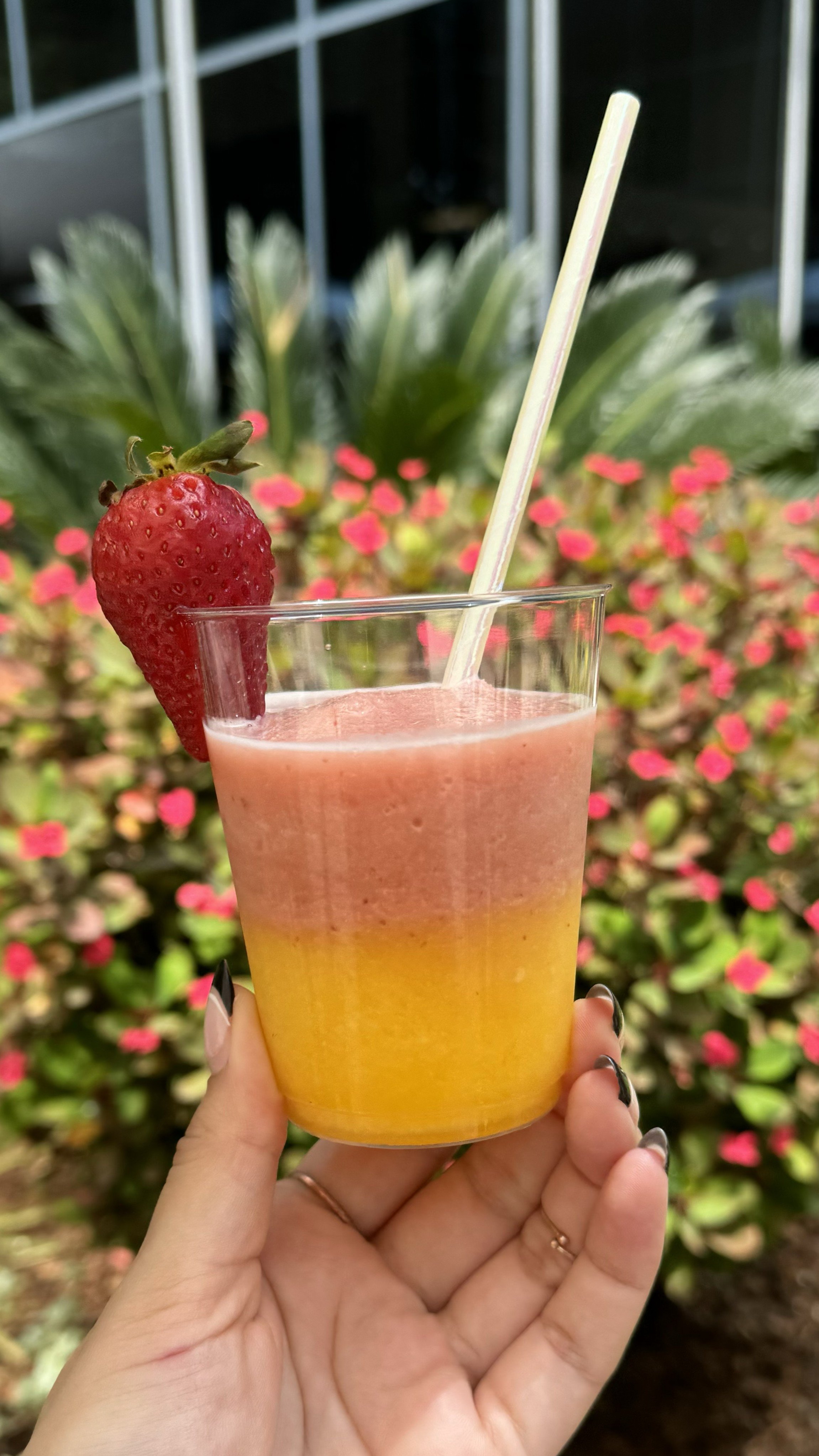 A slushy cup with strawberry and lemonade slush, a straw, a half cut strawberry, held by a hand.