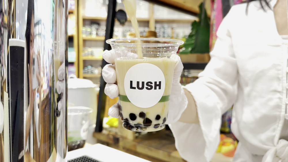 Boba tea poured from a bar tap into a cup full of boba pearls, with a LUSH cosmetics logo on the cup.