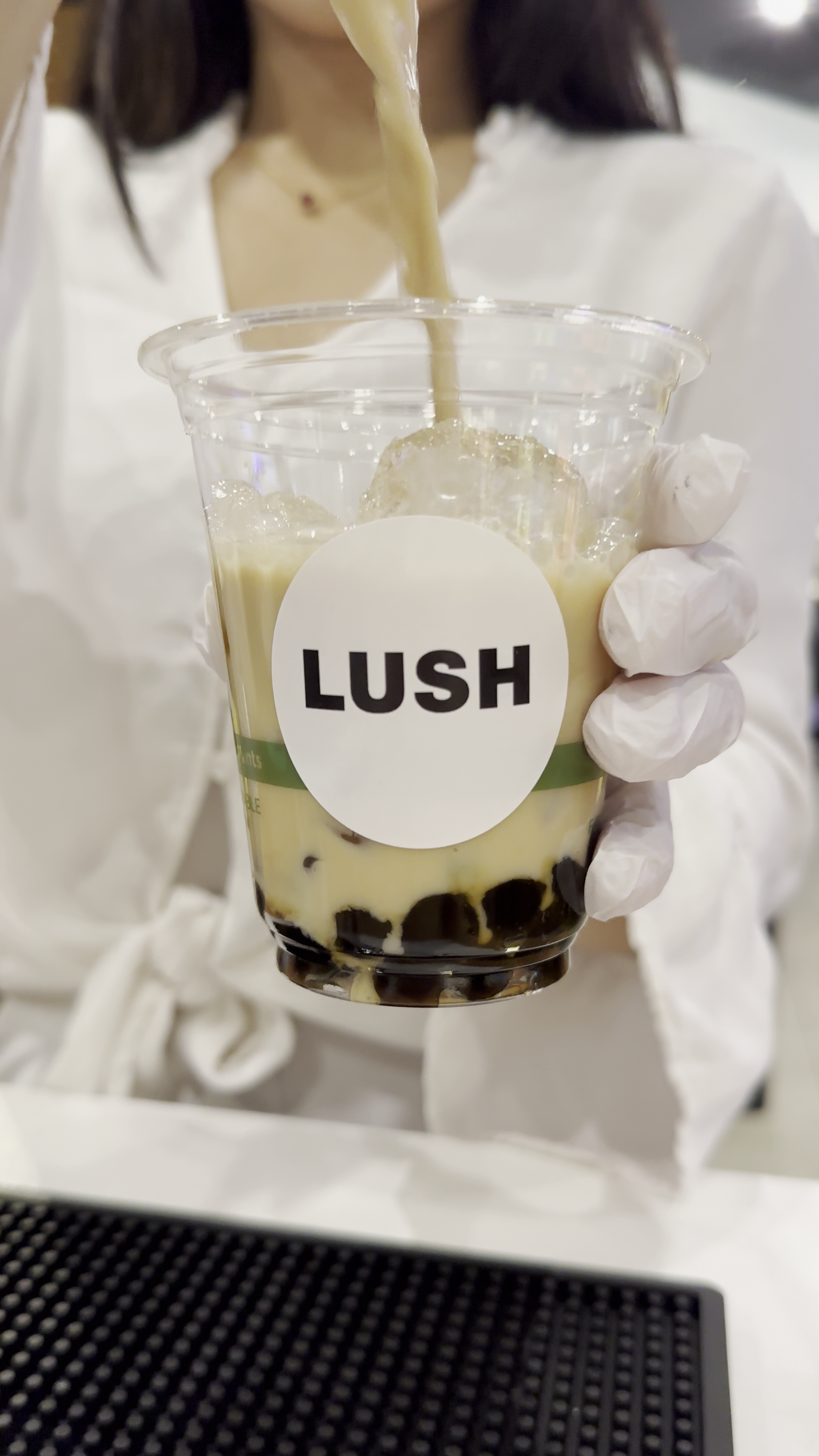 A close up of boba tea being tapped into a cup with a custom LUSH logo and boba pearls sitting at the bottom of the cup