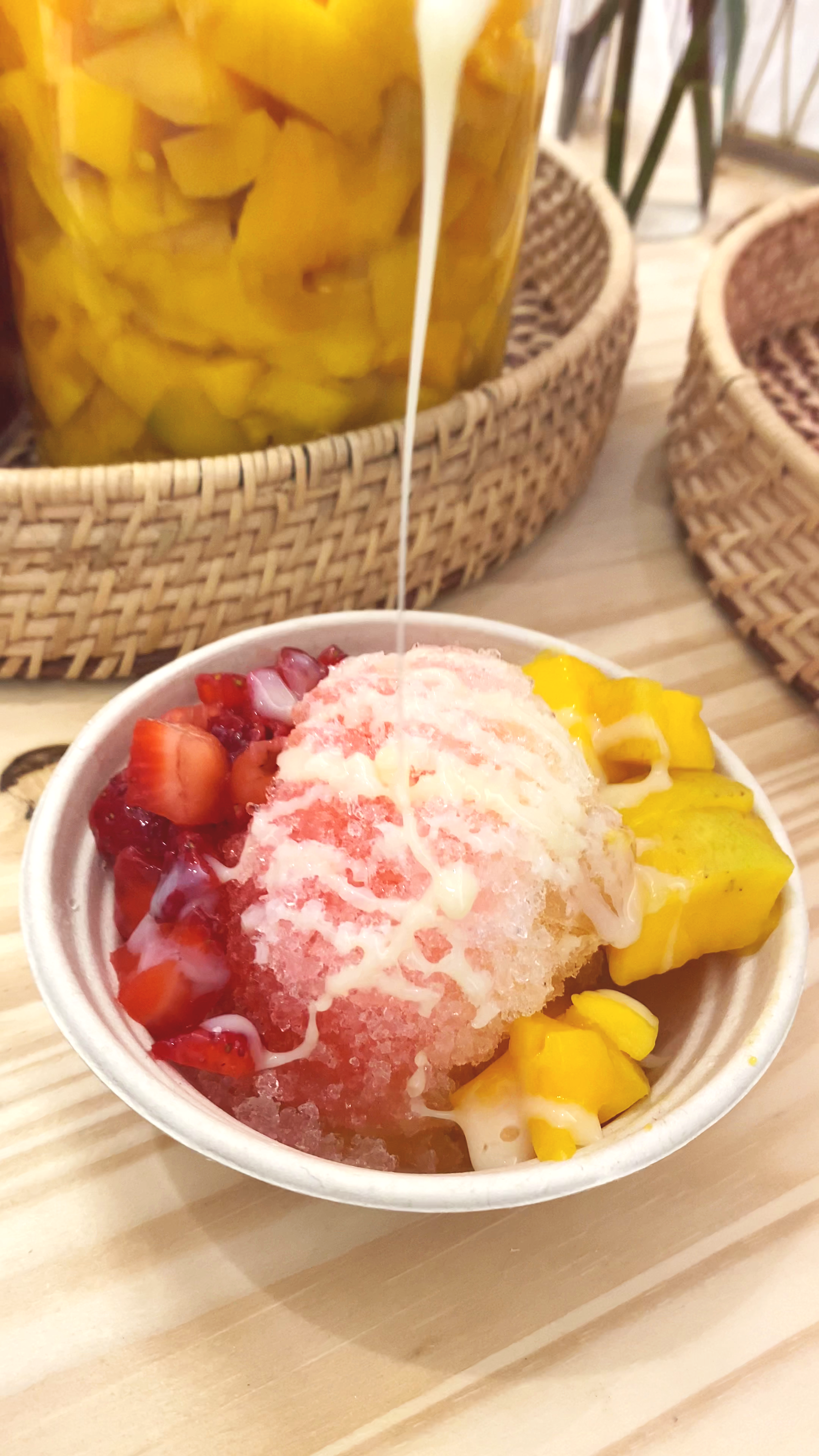 Sweet condensed milk being poured over a shaved ice bowl full of cut strawberries and mangoes at a jolly sheep event