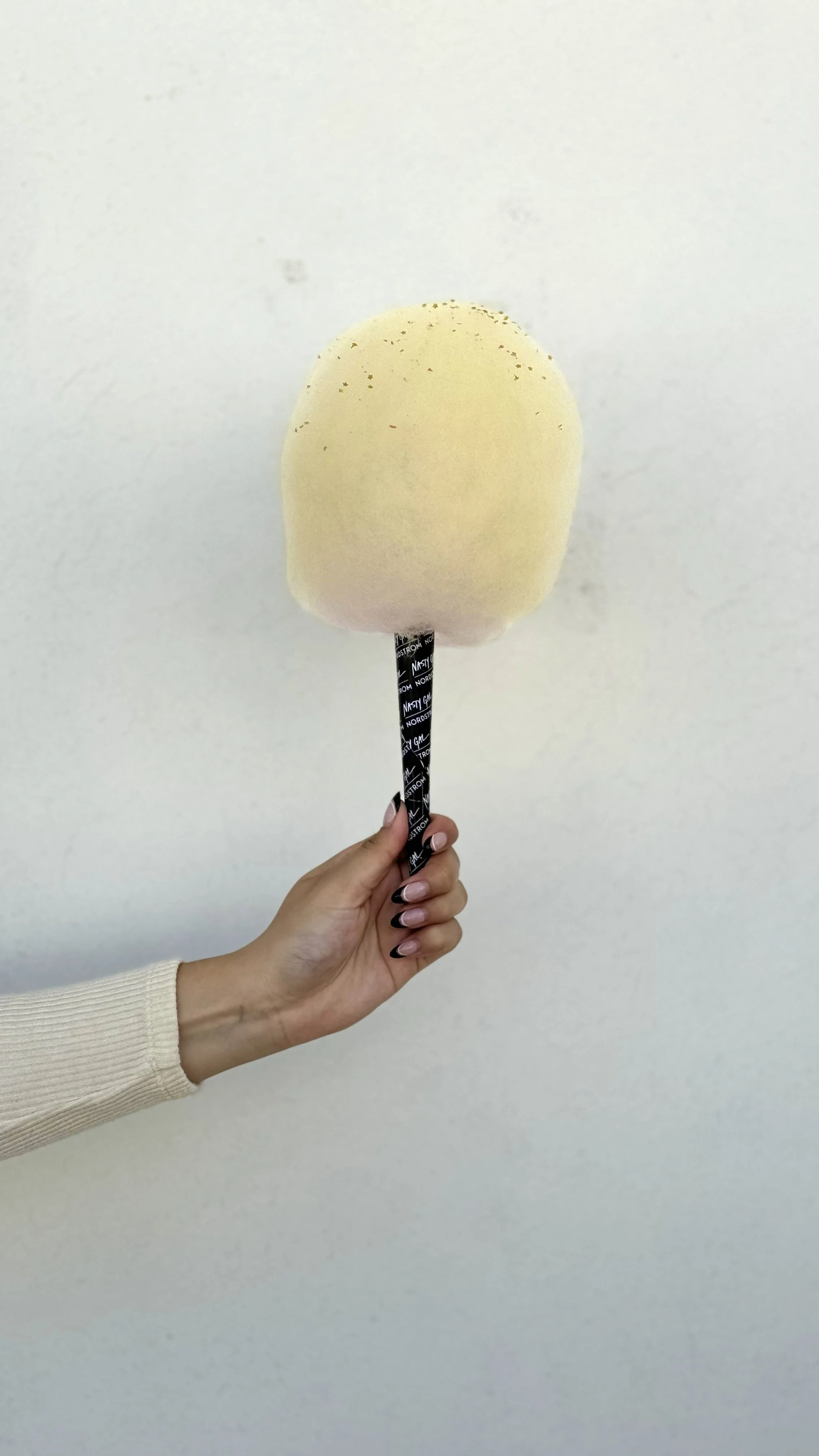 a hand holding up a cotton candy with toppings sprinkled on top