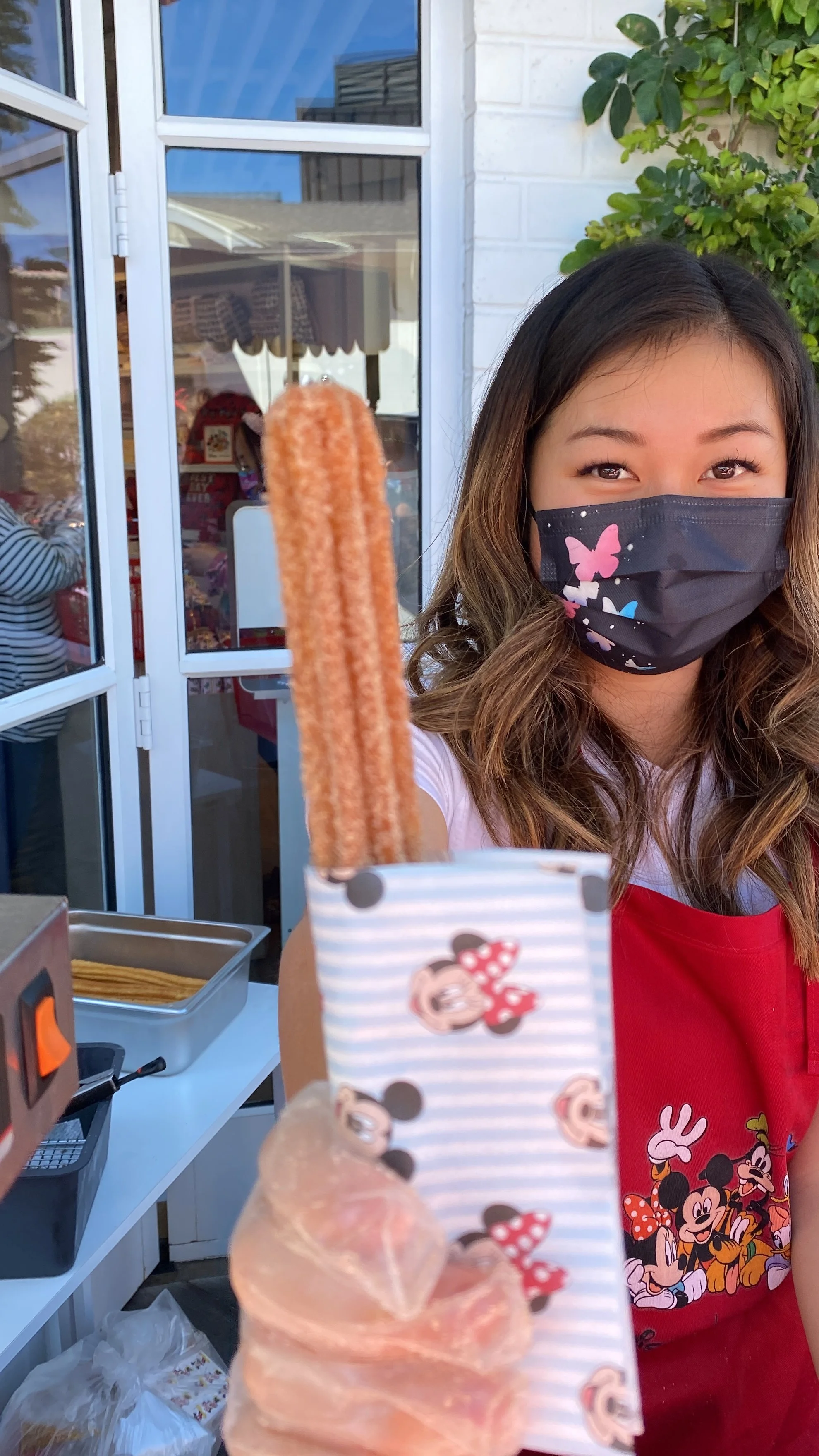 A Jolly Sheep churro attendant handing out a churro in a mickey mouse tissue paper