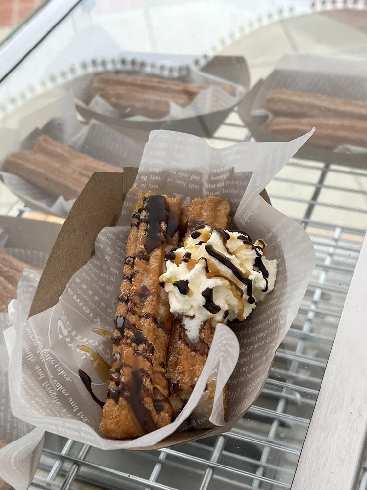 A tray of churros topped with whipped cream and chocolate drizzle.