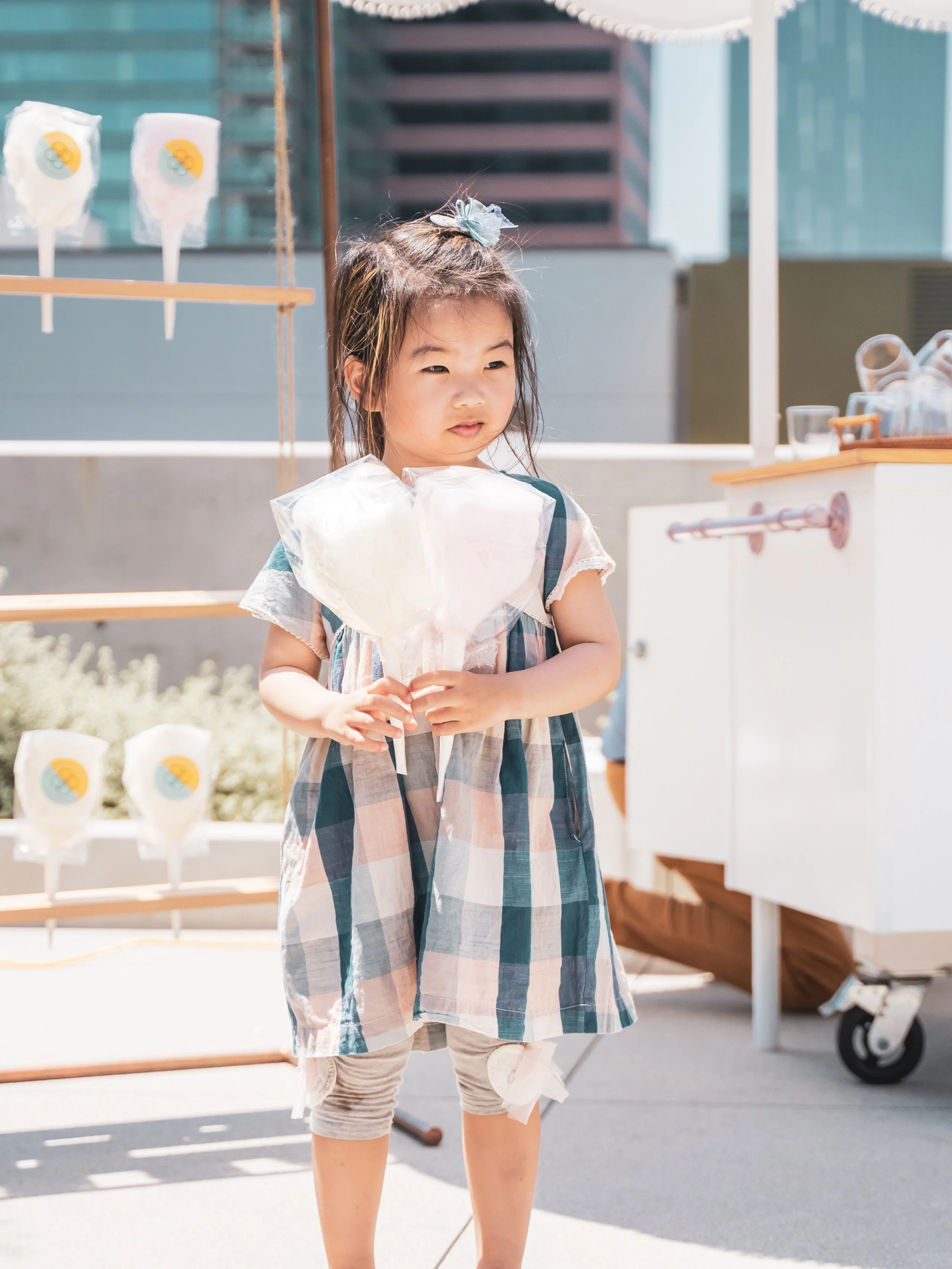 a girl holding two cotton candy favors with a packaged display and cart behind her