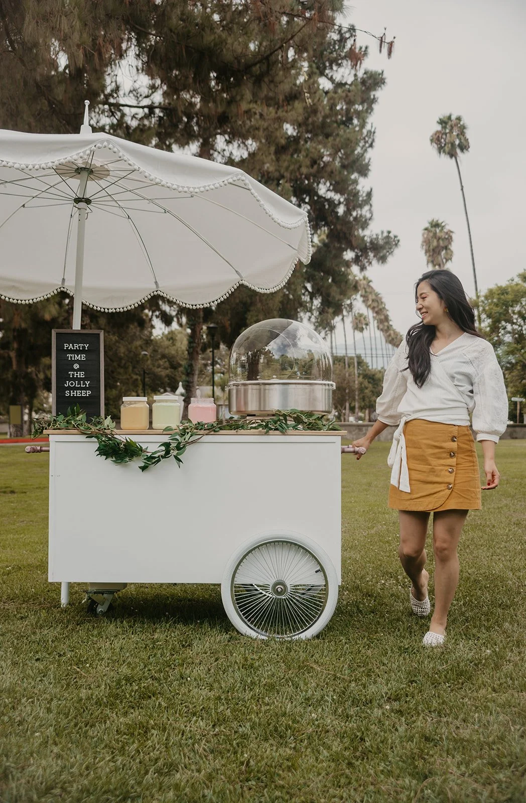 a girl standing next to a cotton candy cart holding the handle and smiling