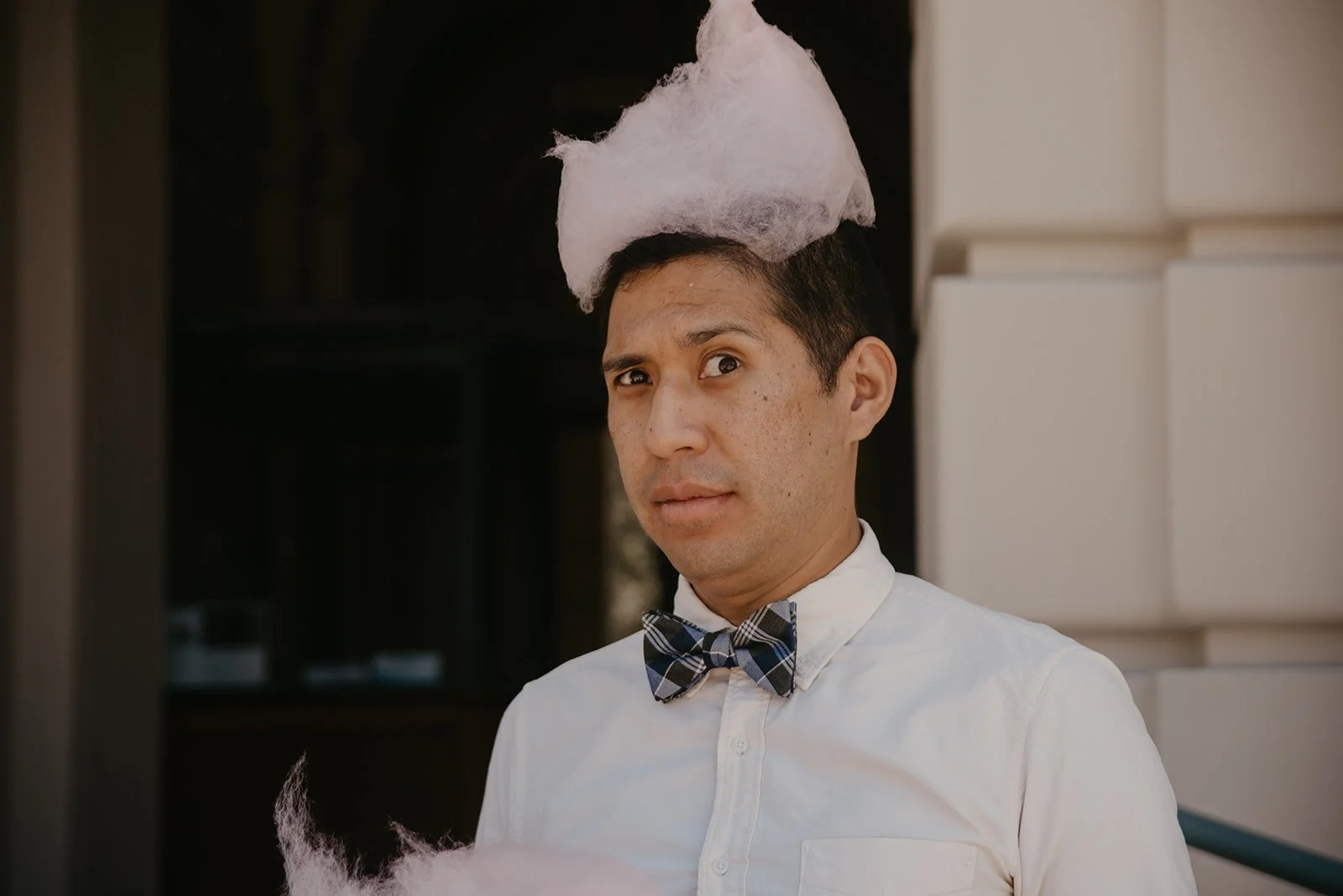 Man with a bow tie staring curiously with a fluff of cotton candy on his head