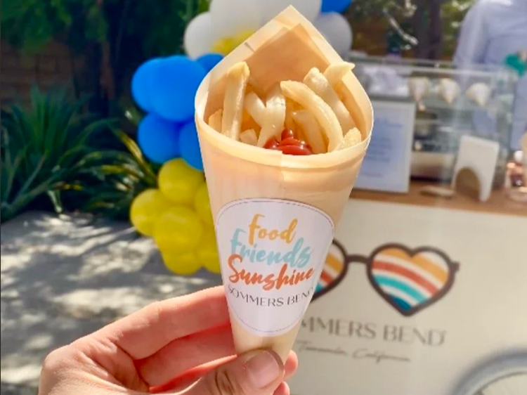 French fries in a bamboo cone, with a french fry cart station behind.