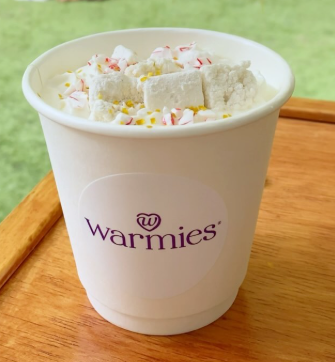 A hot chocolate cup with a custom Warmies label and The Jolly Sheep's in-house marshmallows cut to small squares visible in the cup