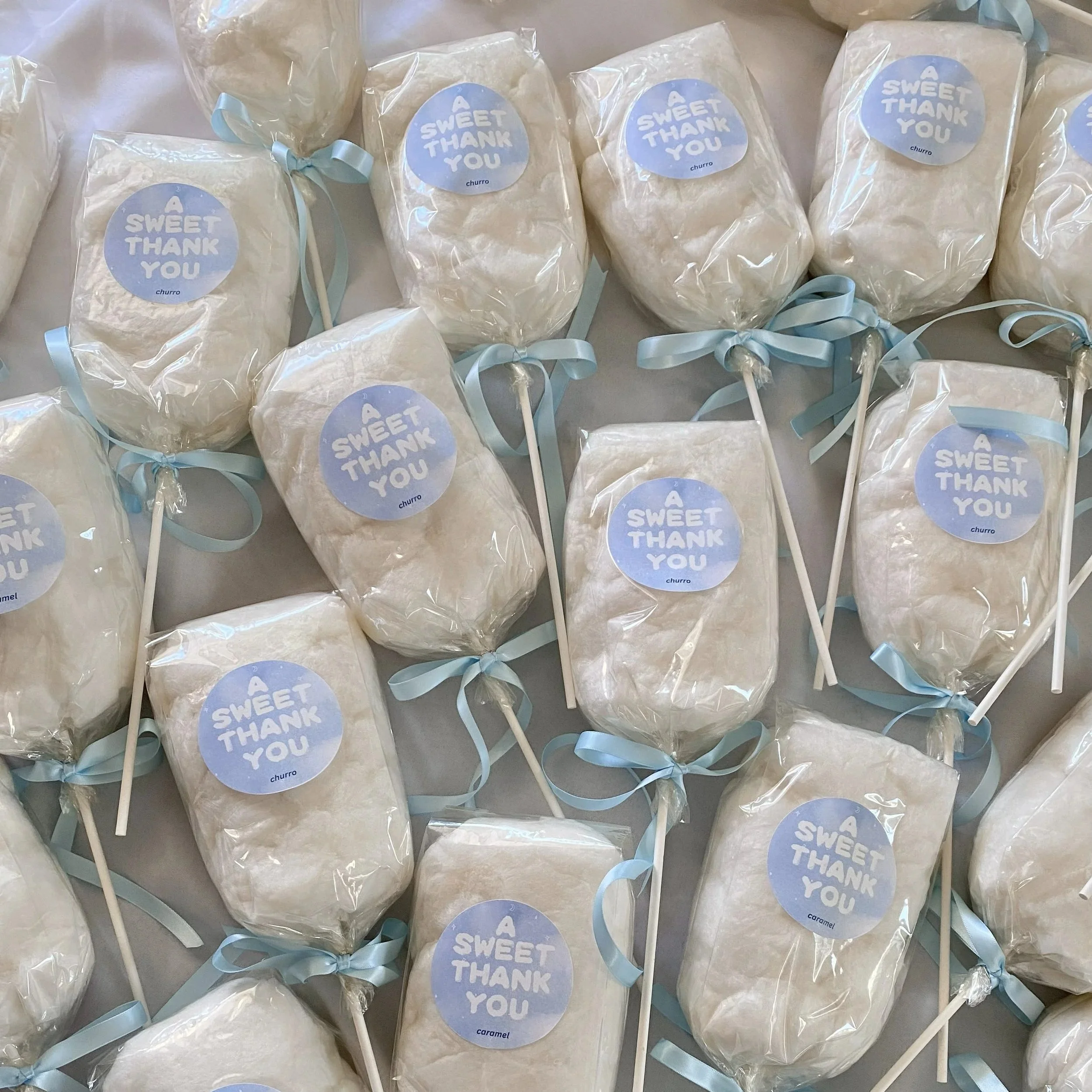 a display of many cotton candy on a stick favors with satin ribbon ties