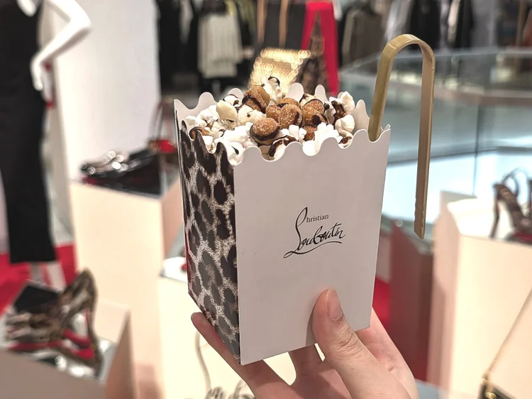 A custom Christian Louboutin popcorn box filled with popcorn, peanuts, chocolate drizzle and fancy tongs.