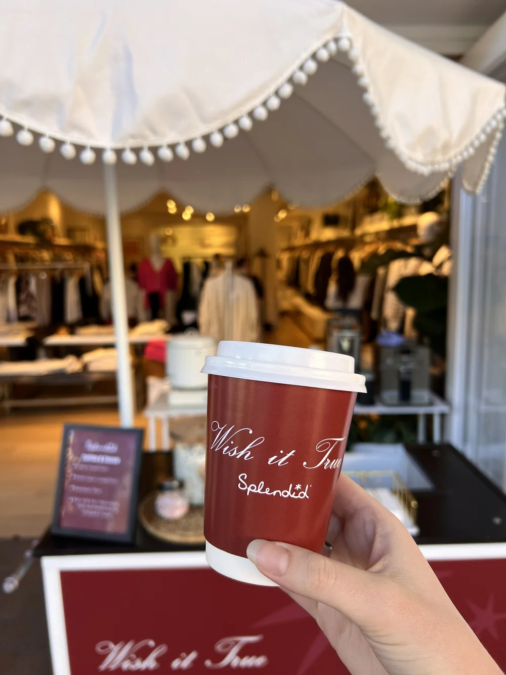 A custom coffee cup held up in front of a Splendid store at Fashion Island.