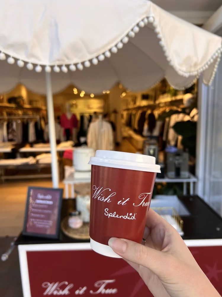 A custom coffee cup held up in front of a Splendid store at Fashion Island.