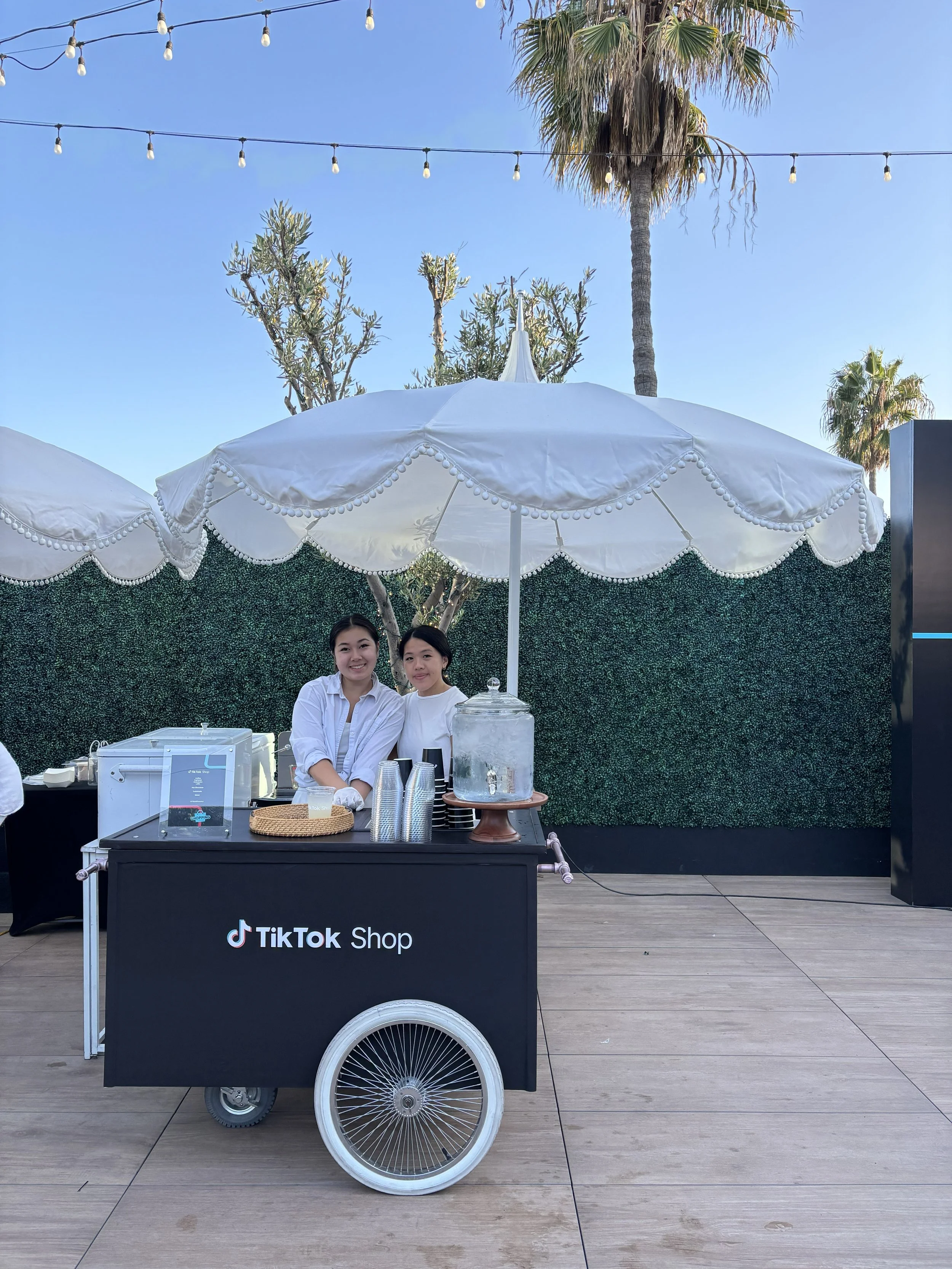 two servers in front of a tiktokshop branded lemonade cart for an event