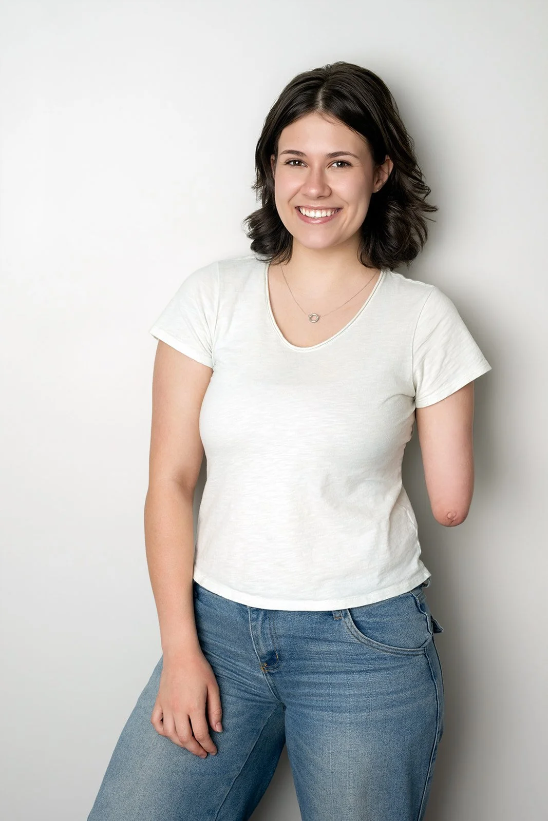 Jordan smiles while standing near a white wall, wearing an off-white shirt and jeans