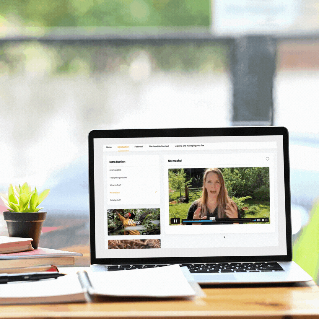 Laptop on a desk displaying an online educational video about fire safety, with notebooks and a potted plant beside it.