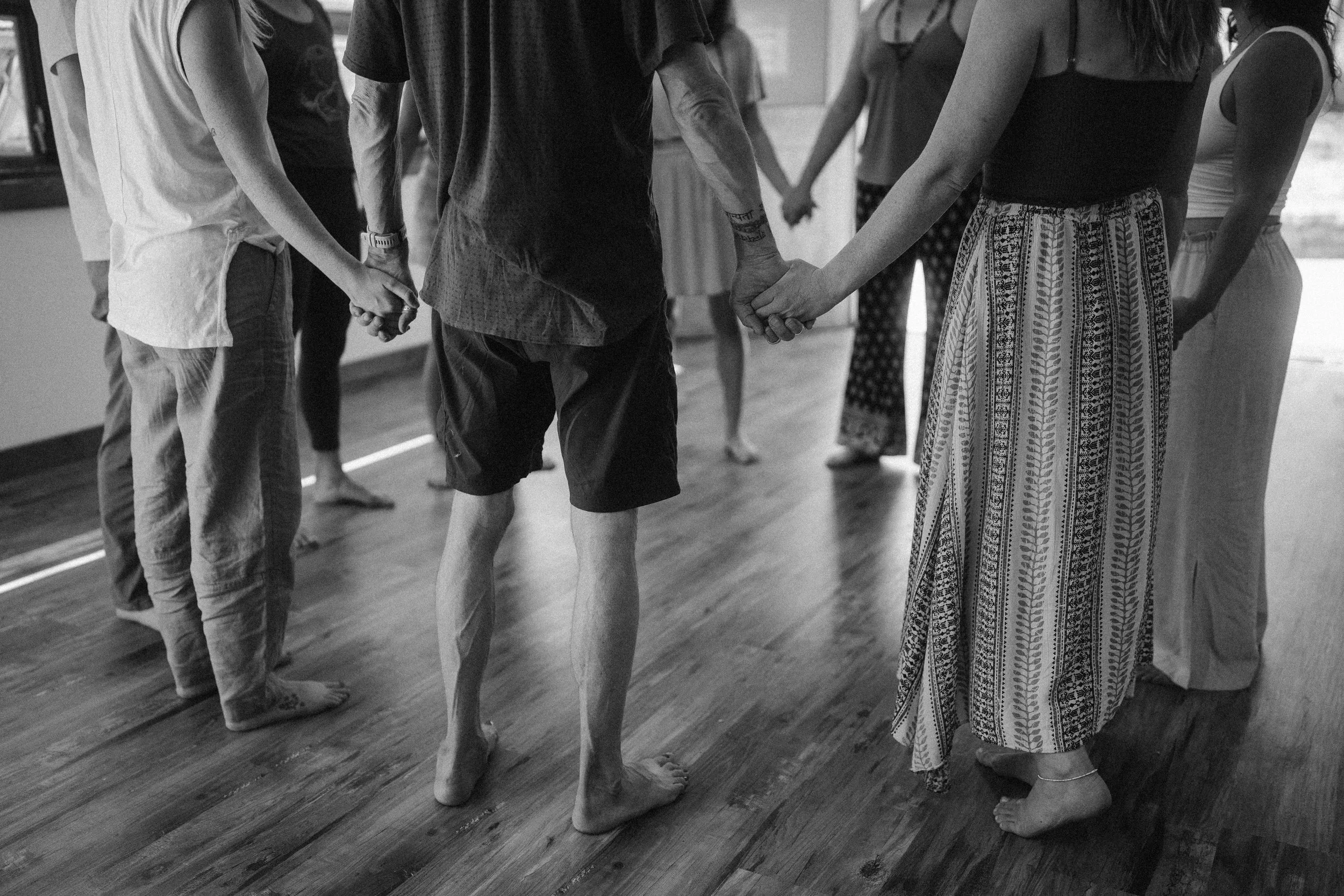 A group of people hold hands in a circle with a black and white overlay.