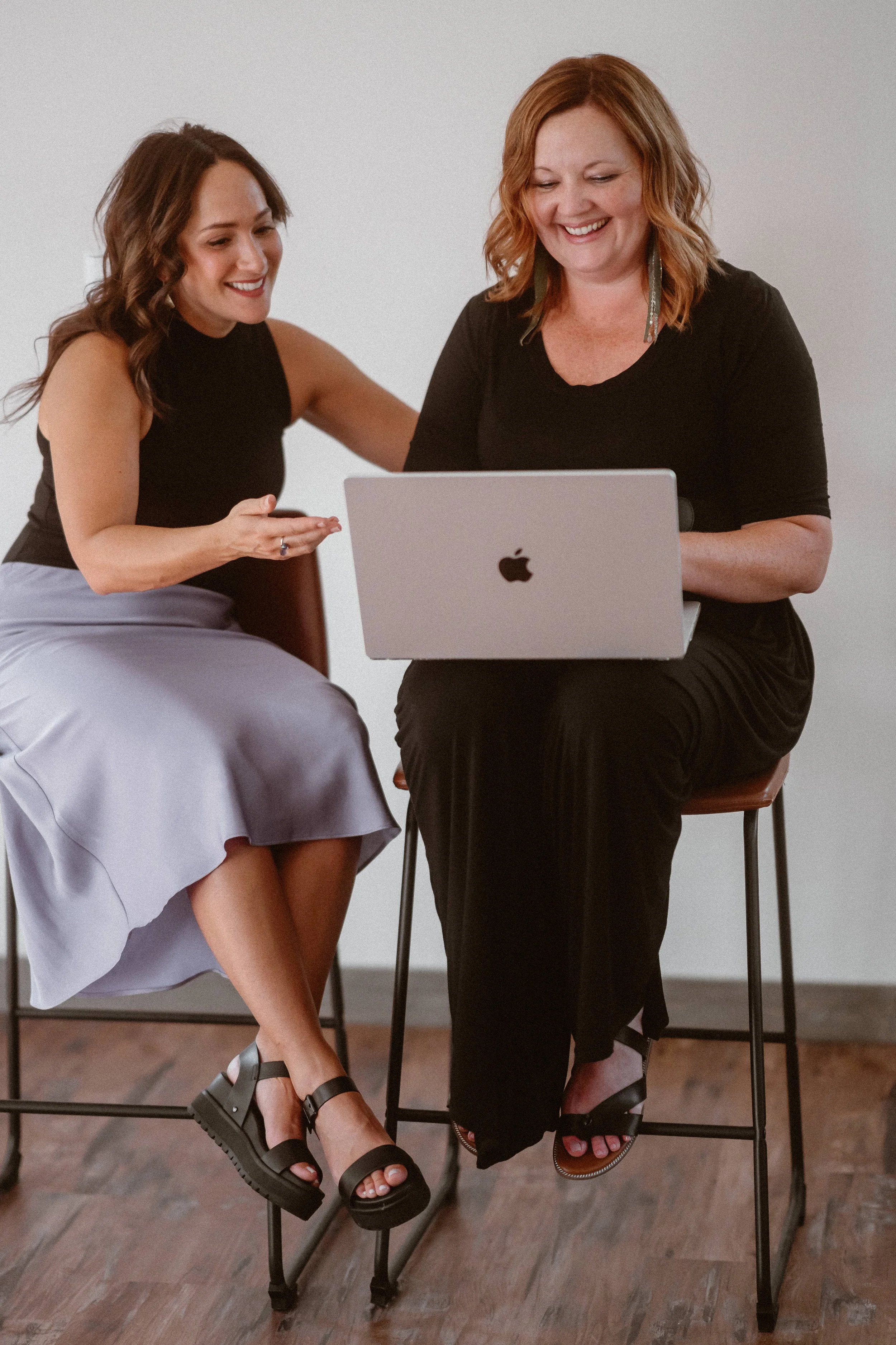 Dori Lewis sits on a stool smiling talking to another person who is on their computer.