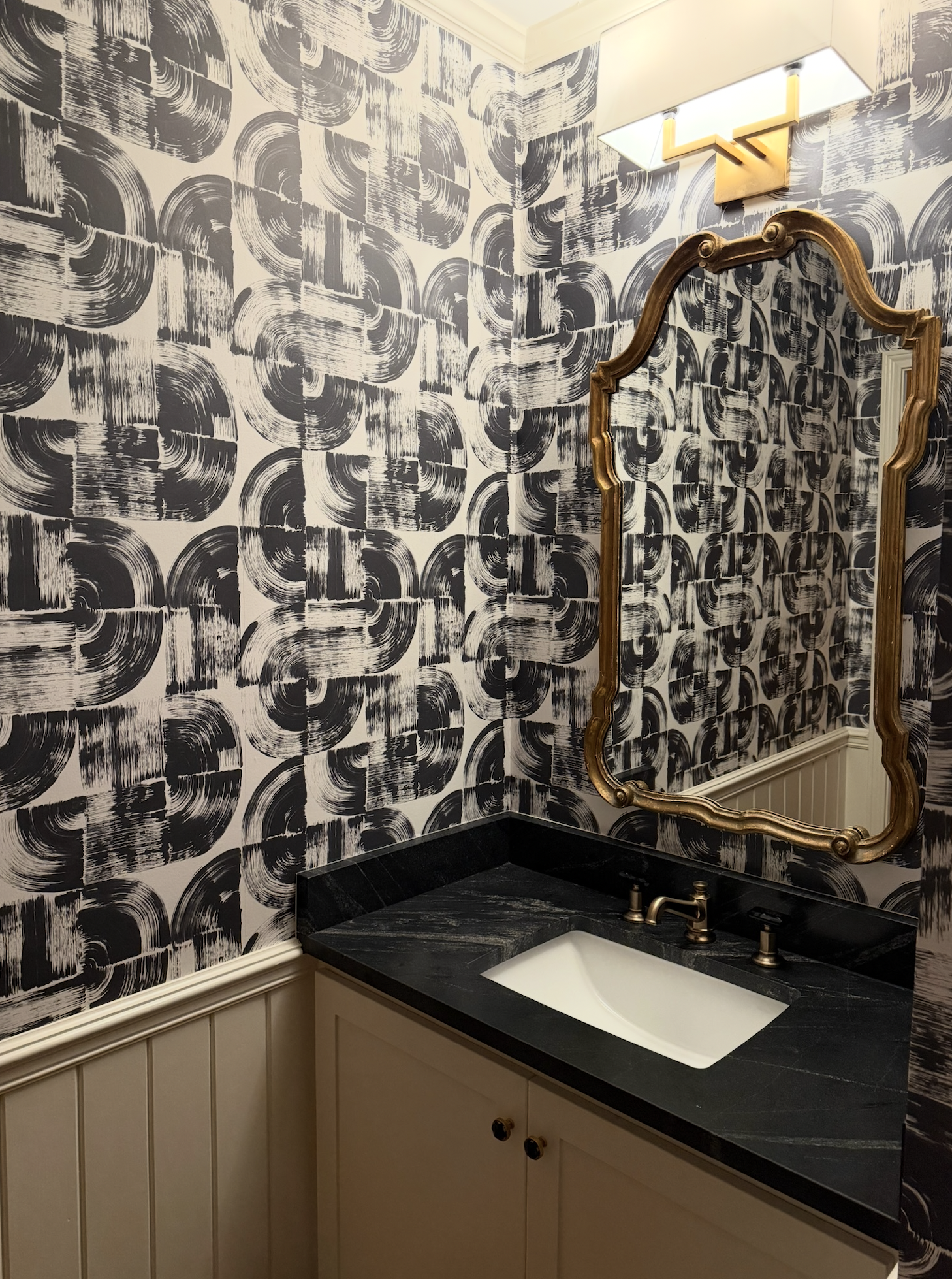 Black and white abstract wallpapered bathroom with gold ornate mirror and fixtures