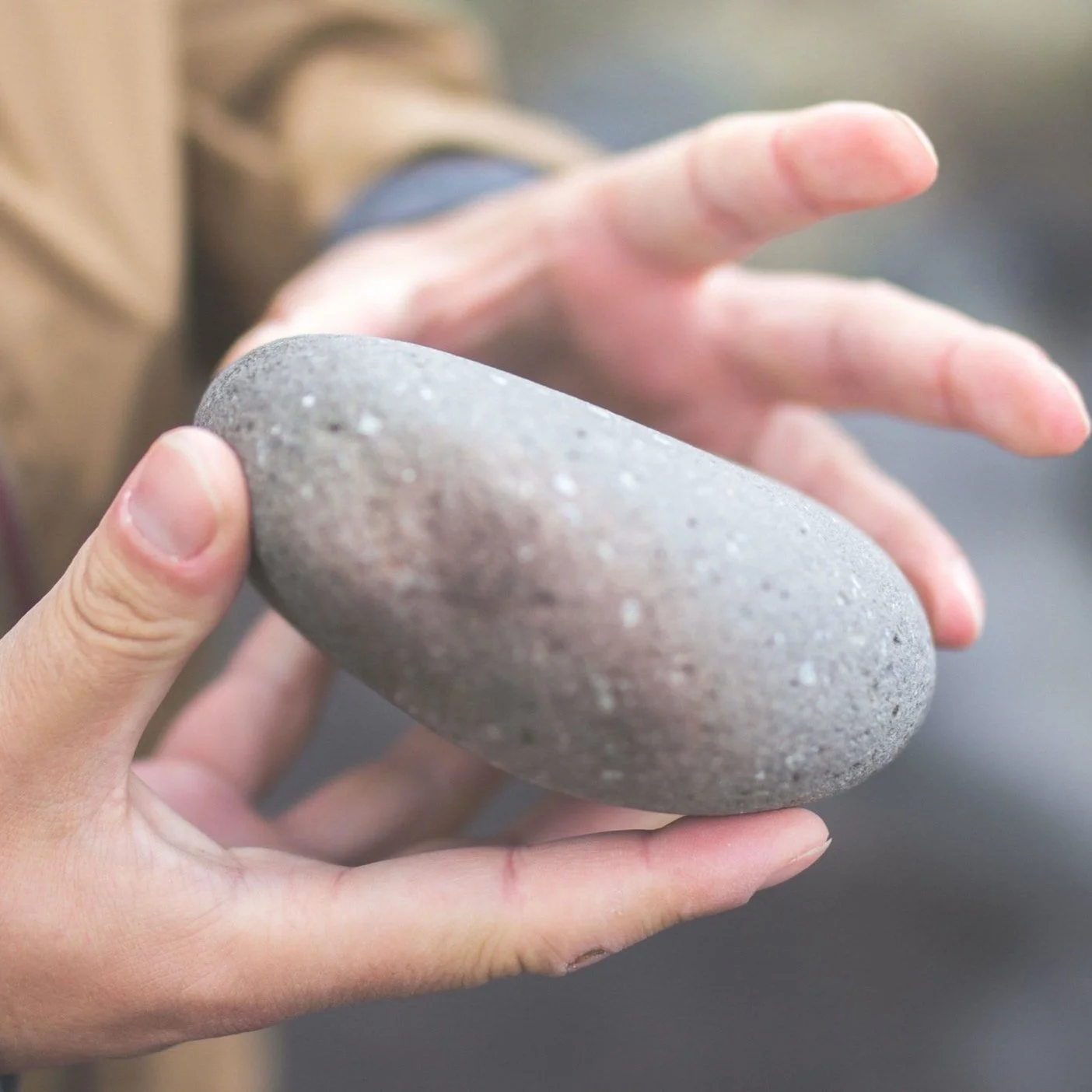 Person holding and inspecting a smooth gray stone with one hand.