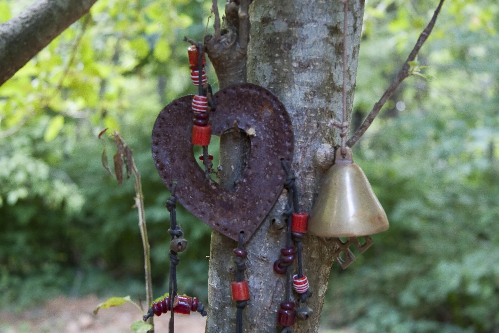 bell, beads, and rusty heart hanging on a tree