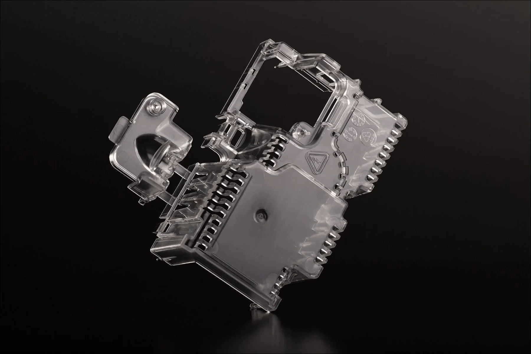 Transparent plastic mechanical component with complex structure displayed against a black background.