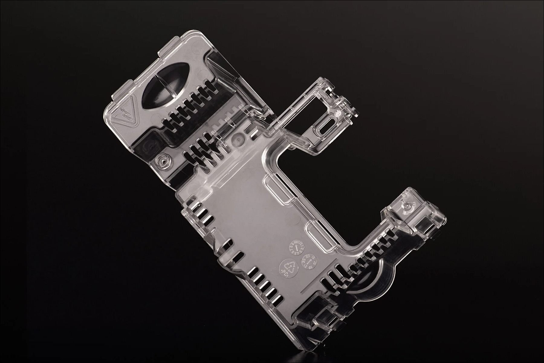 Transparent plastic bracket-like mechanical part with ridges and holes displayed against a black background.