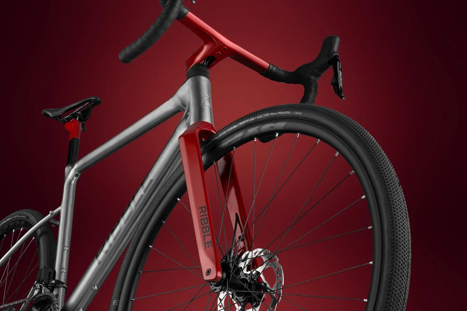 Three-quarter view of the Ribble Allroad's integrated cockpit and metallic red fork on a titanium-colored frame.