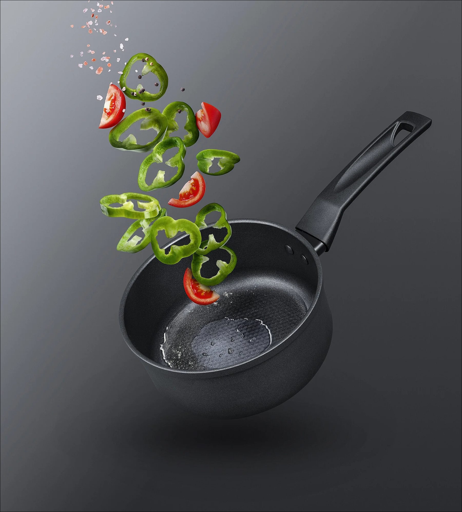 Black frying pan tossing sliced green peppers and red chili peppers into the air against a gray background