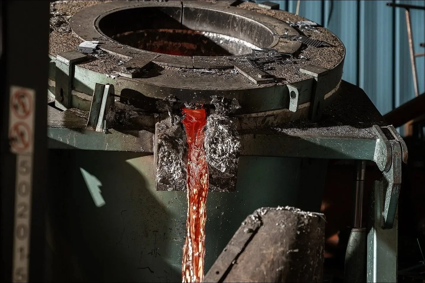 Molten metal pouring from a crucible spout into a mould in a foundry environment.