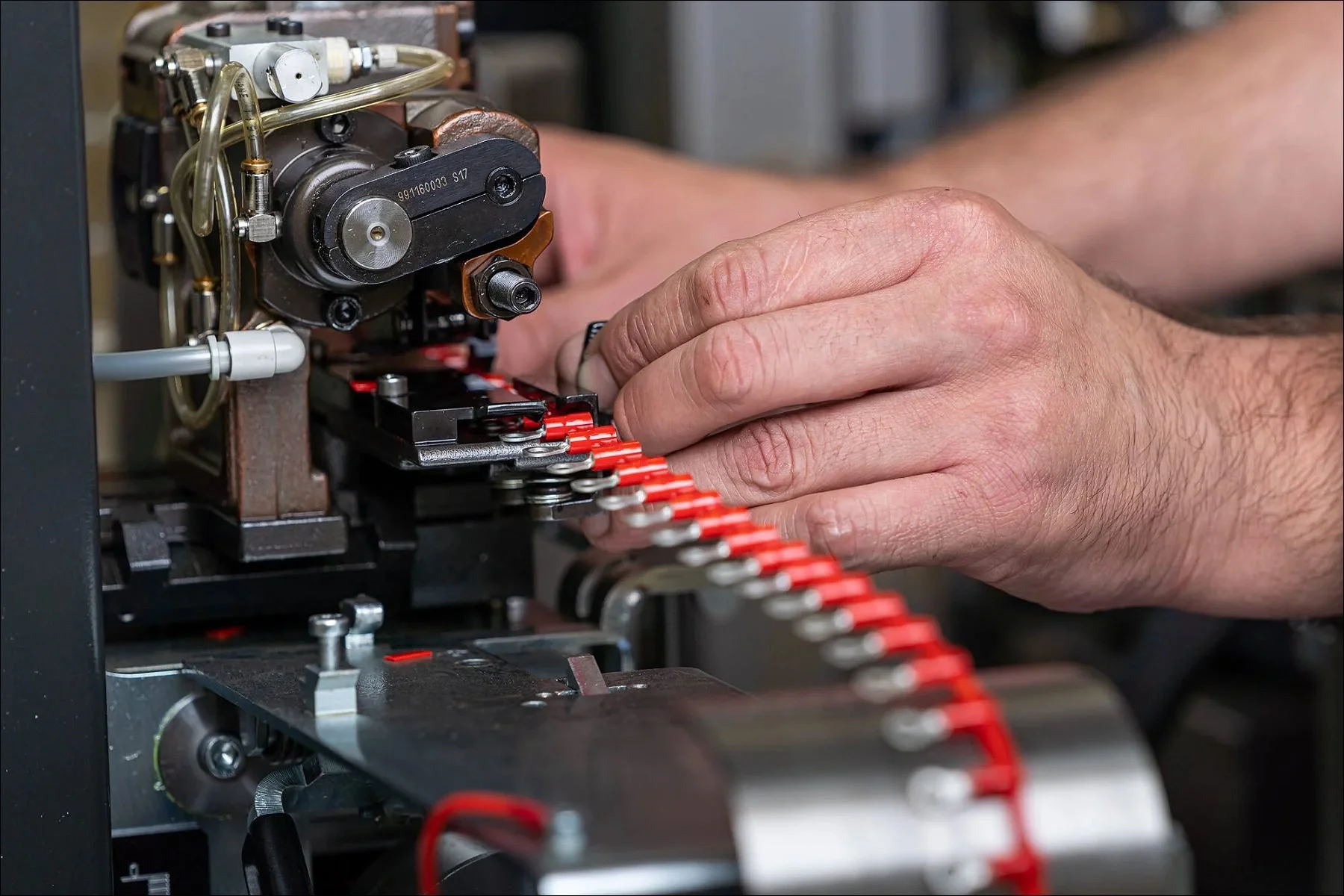 Close-up of a worker's hands guiding a red cable through an industrial machine for processing.