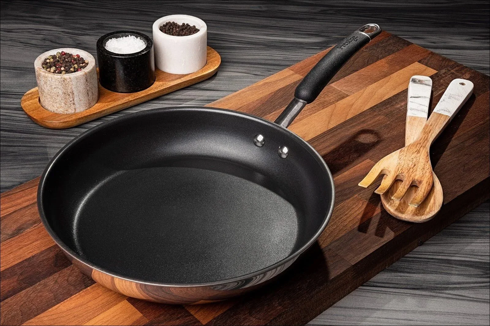 Black frying pan on a wooden cutting board accompanied by wooden utensils and salt and pepper shakers