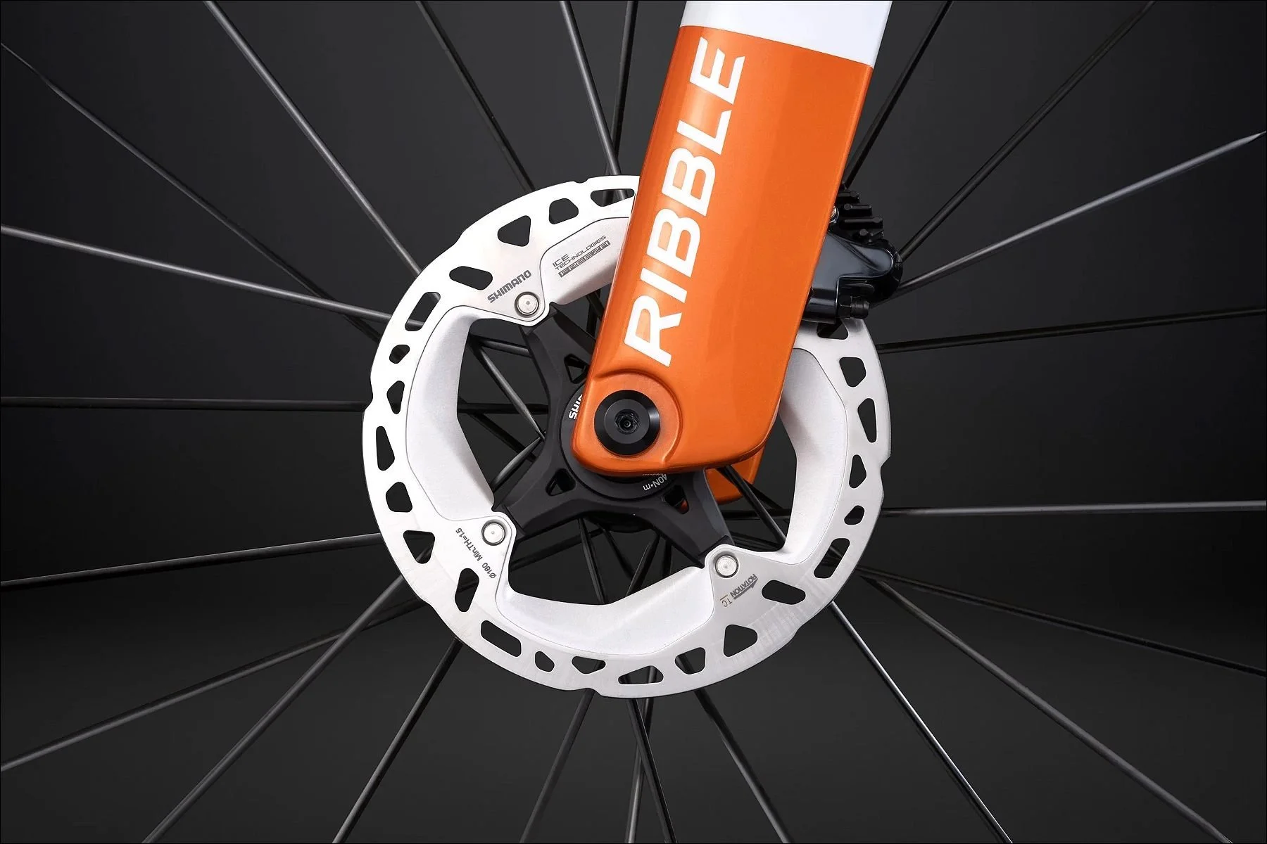 Close-up of a white bicycle disc brake rotor and black wheel spokes with an orange fork featuring Ribble branding.