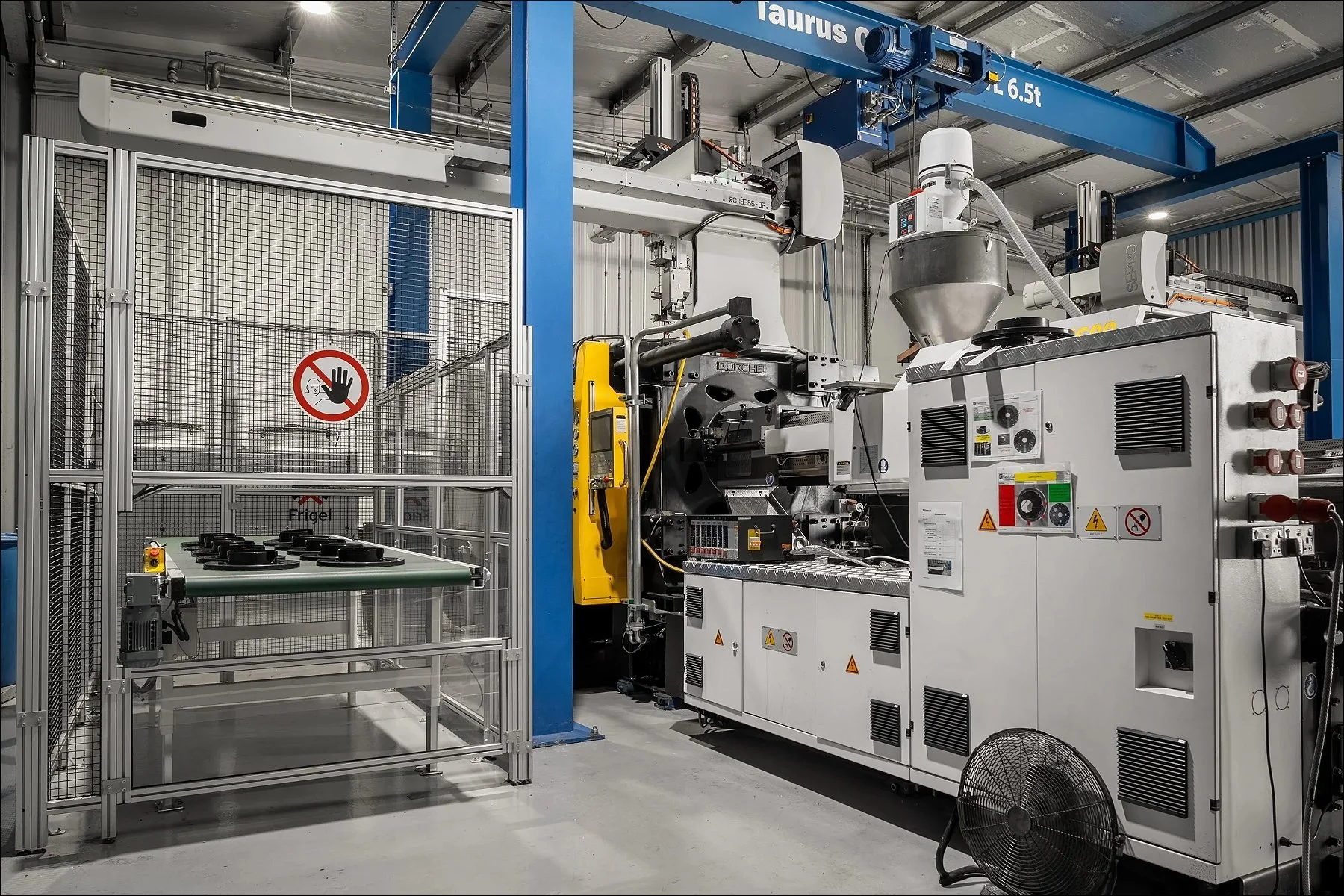 Large industrial machine and enclosures on a factory floor with blue overhead structures.