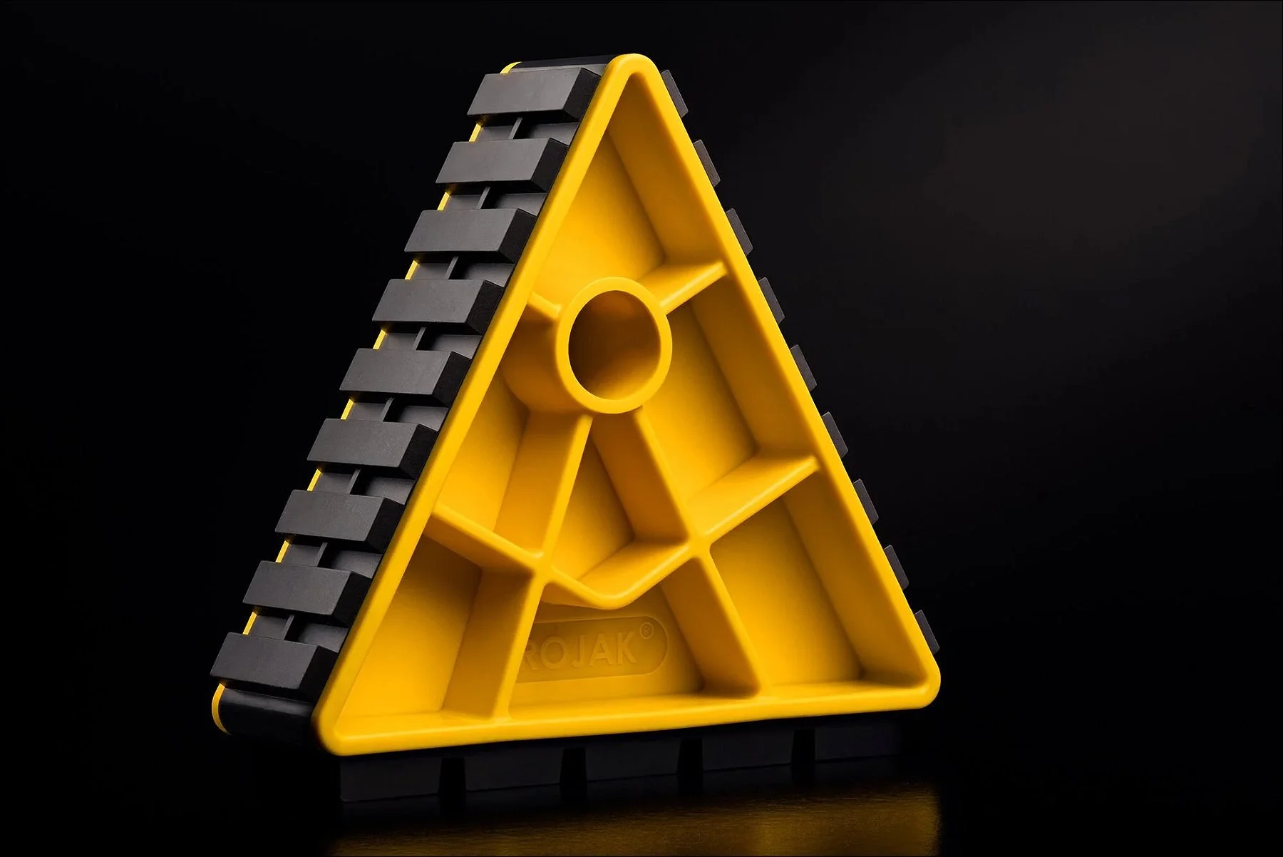 Bright yellow triangular plastic object with a ridged side and central hole against a dark background.