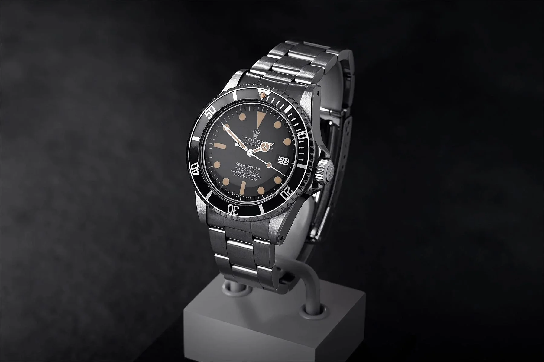 Silver wristwatch displayed on a gray pedestal against a dark background