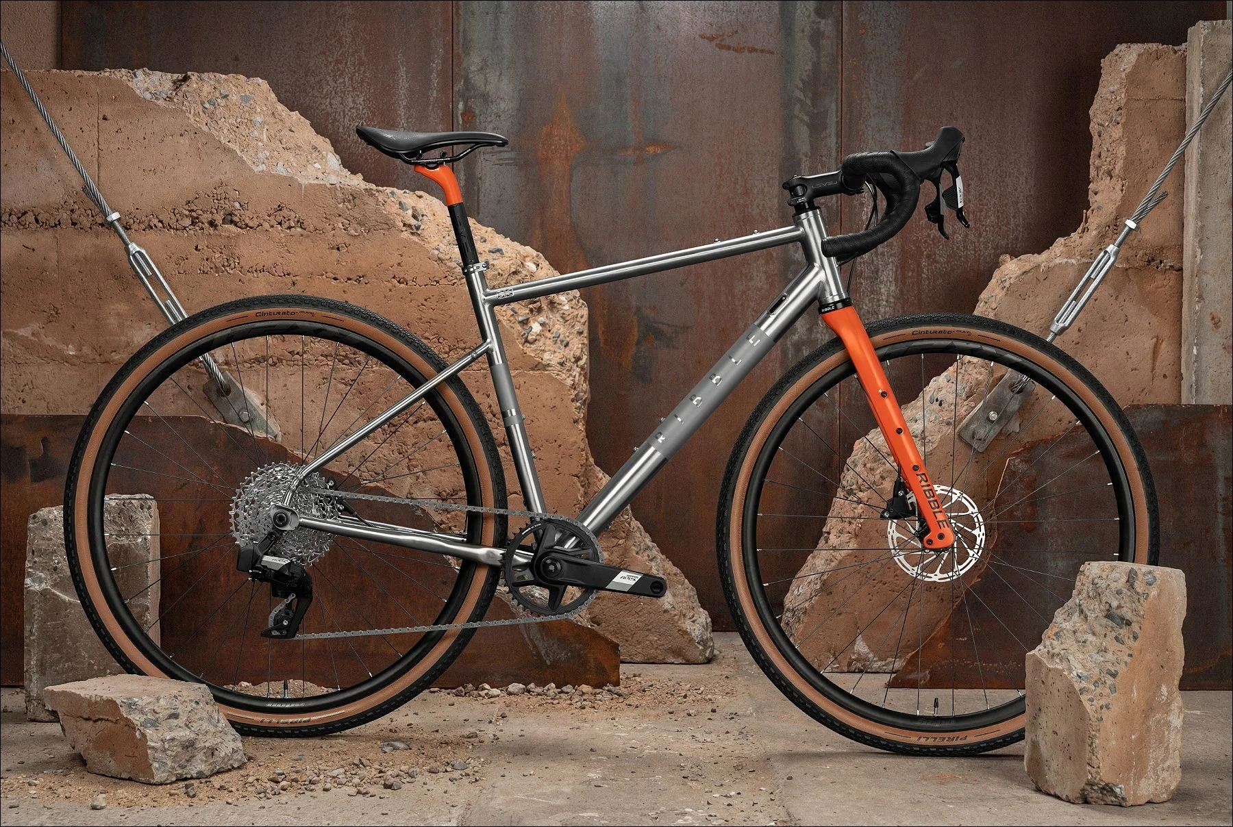 Grey bicycle with orange fork displayed among broken stone and concrete pieces in an industrial setting.