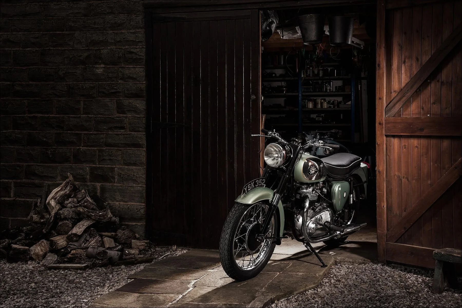 Vintage green motorcycle parked inside a rustic workshop with wooden doors.