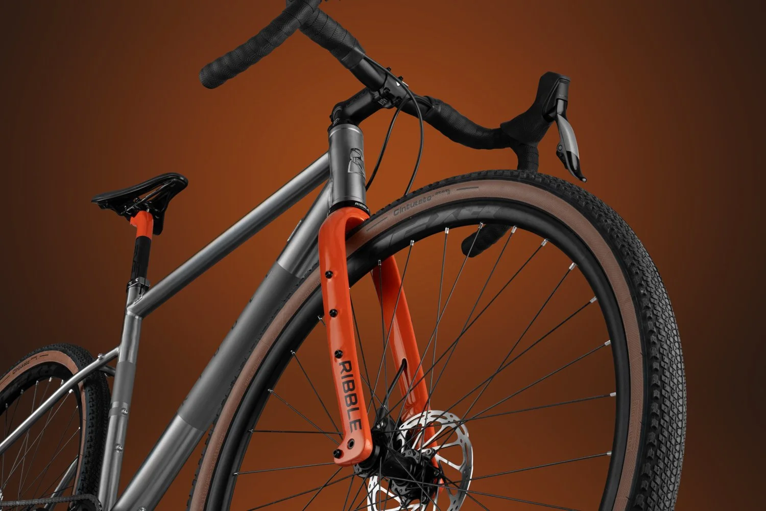 Three-quarter view of the Ribble gravel integrated cockpit and metallic orange fork on a titanium-colored frame.