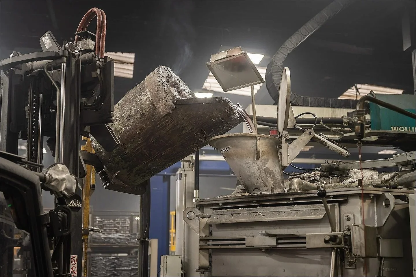Large industrial machinery hoisting a heavy metal container in a foundry or manufacturing facility.
