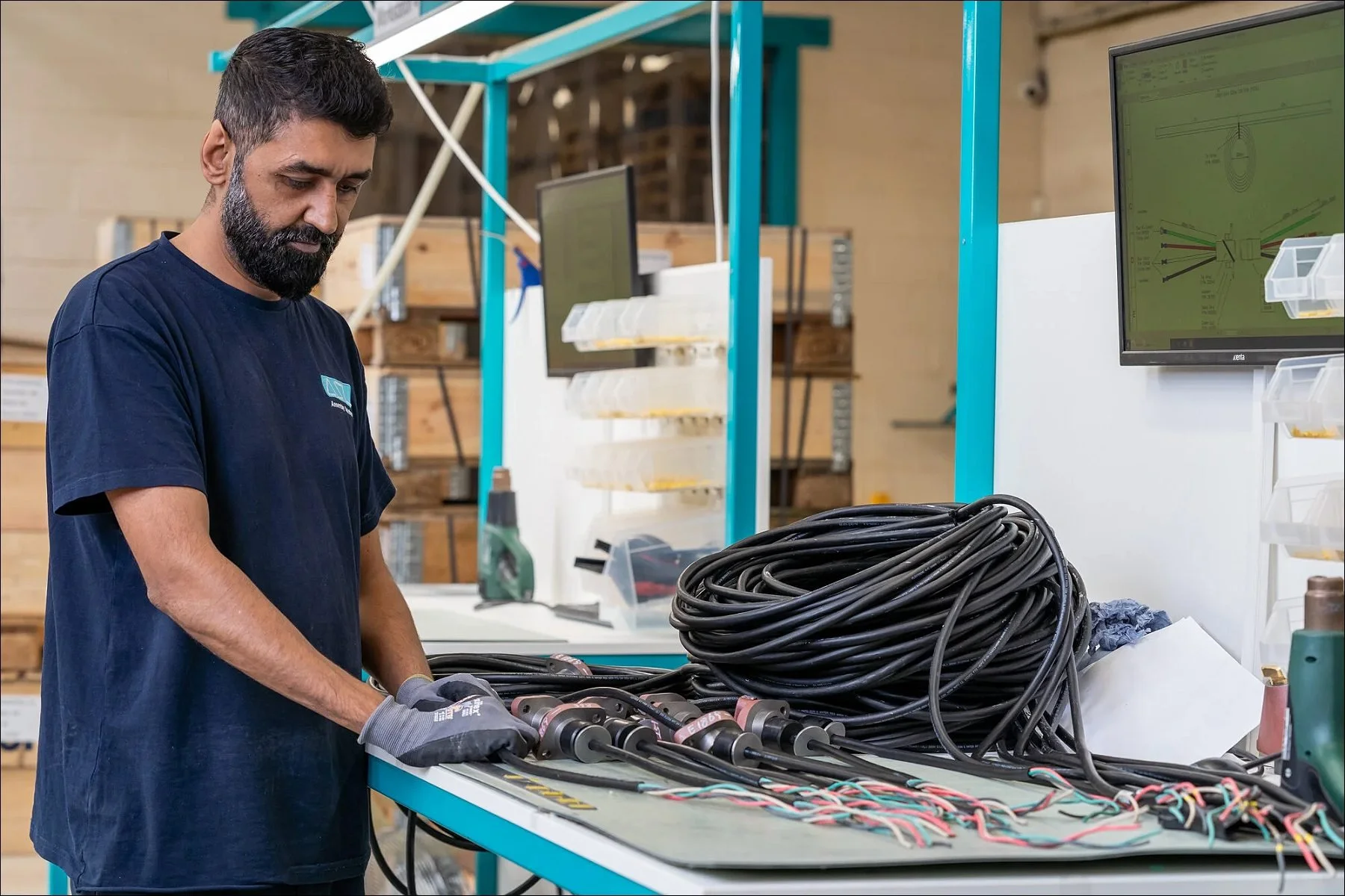 Factory worker handling bundles of cables at a workstation with wiring harnesses.