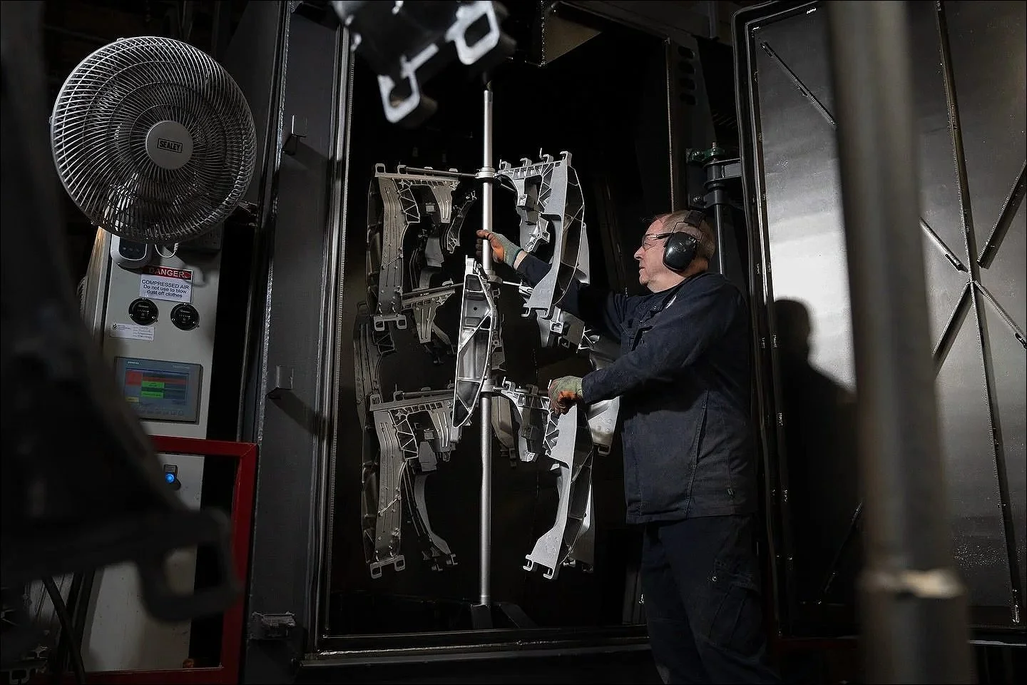 Industrial worker monitoring multiple metal parts hanging inside a large industrial booth.