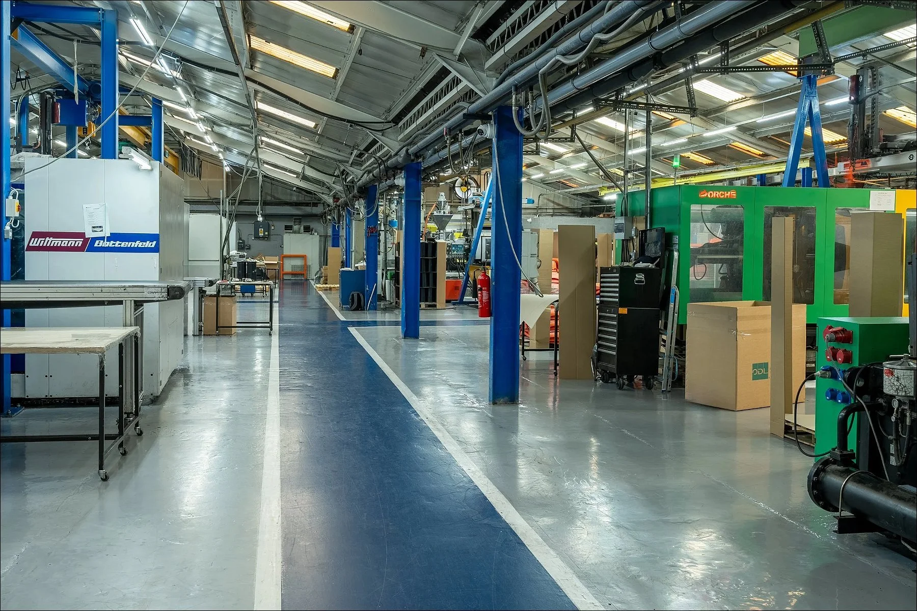Wide view of a manufacturing facility aisle lined with machinery, blue support beams, and workstations.