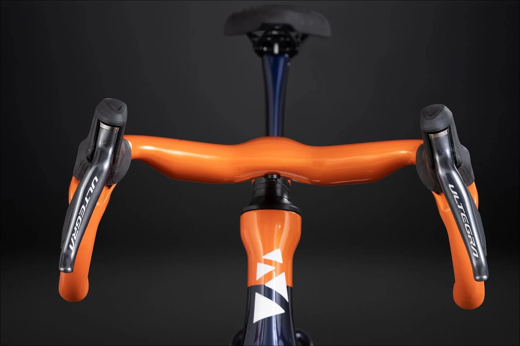 Front view of an orange aerodynamic bicycle handlebar with integrated stem against a dark background.
