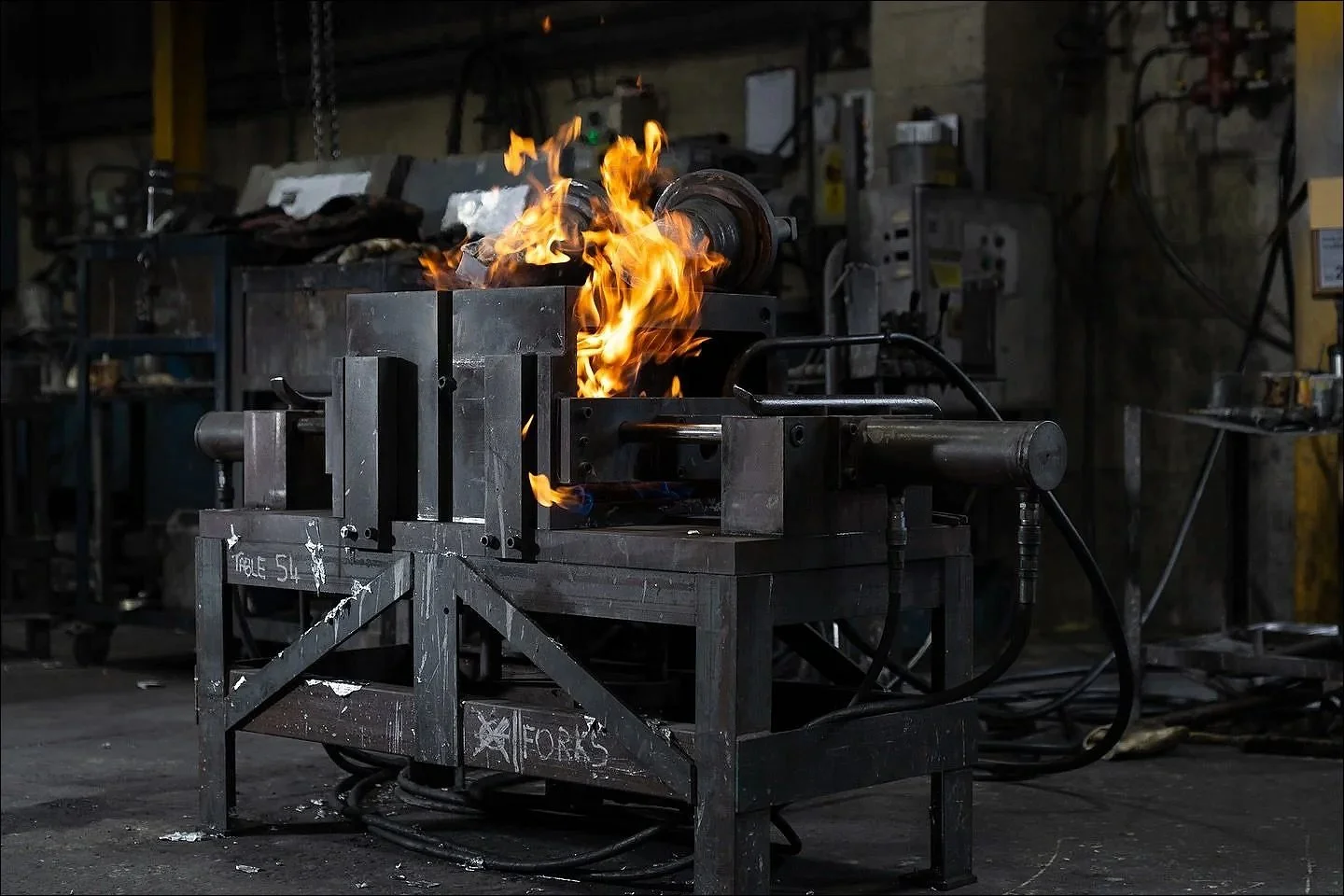 Industrial workstation with a small open flame burning atop a metal apparatus used for casting or forging.