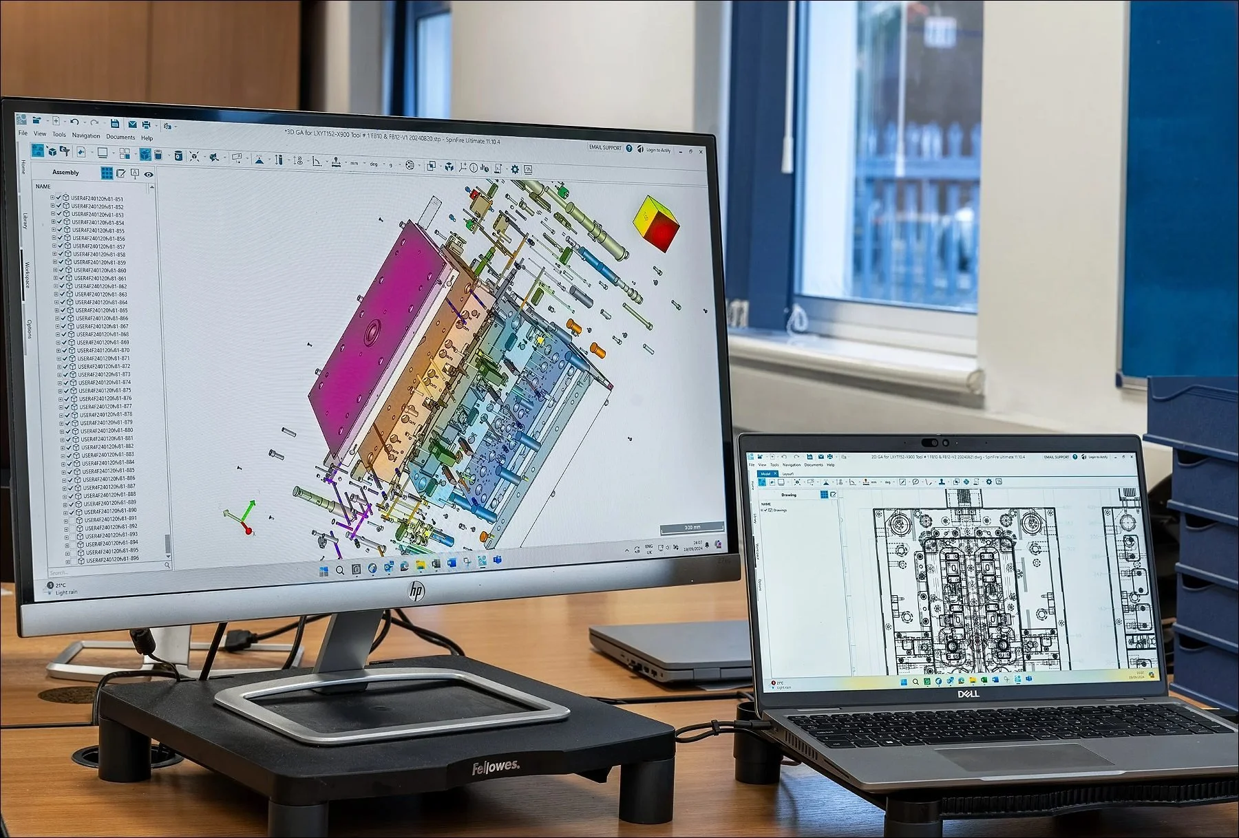 Workstation with a large monitor and laptop displaying engineering CAD diagrams and plans.