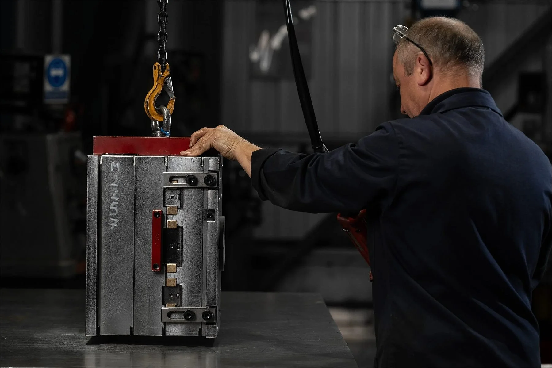 Factory worker using an overhead crane to lift a heavy metal mold in a manufacturing facility.