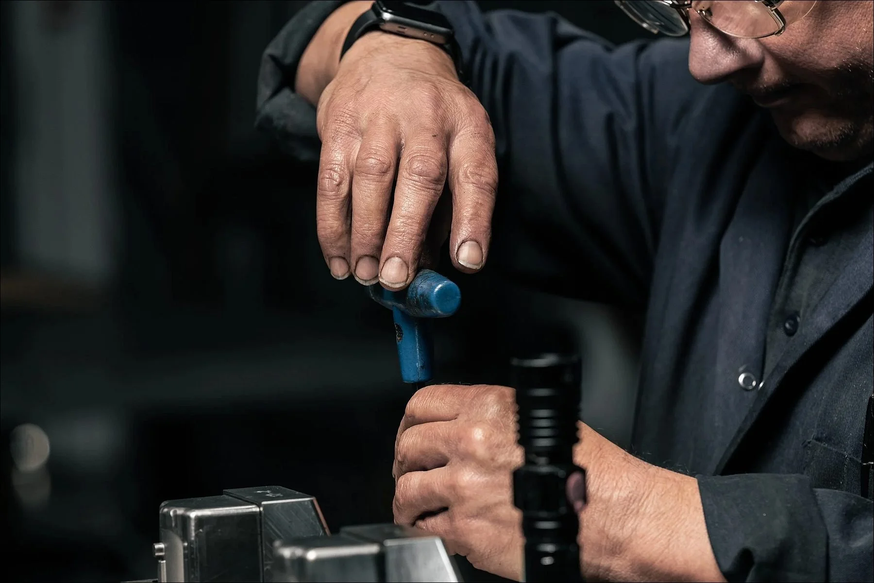 Factory worker using a tool with a blue knob to adjust equipment at a workstation.