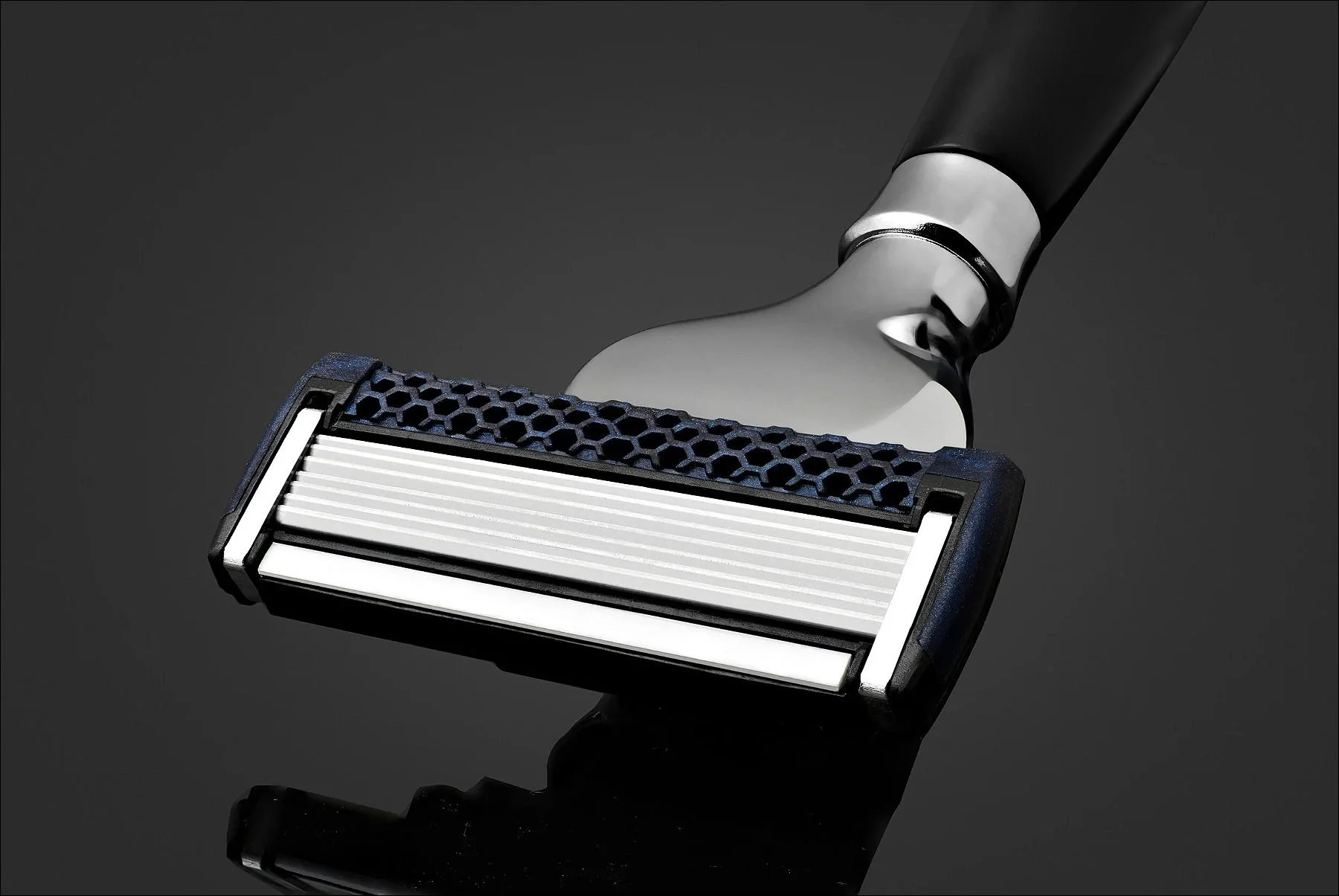 Close-up of a razor head with a dark handle on a reflective black surface